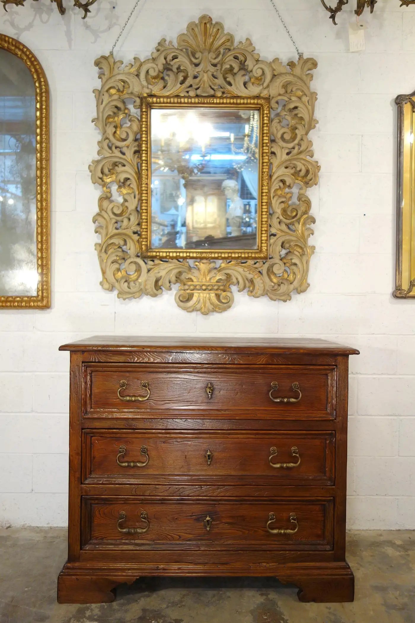 Wooden dresser with ornate gold mirror above it against a white wall.
