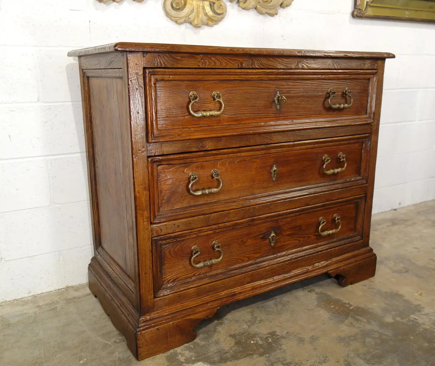 Wooden dresser with three drawers against a white wall.