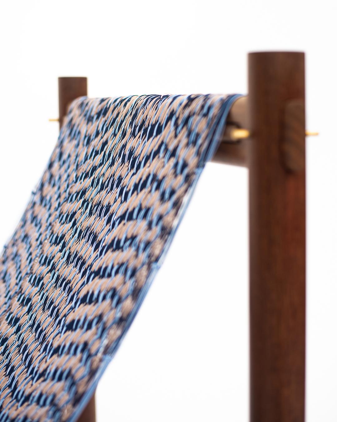 Textile with blue and beige pattern draped over a wooden rod on a white background