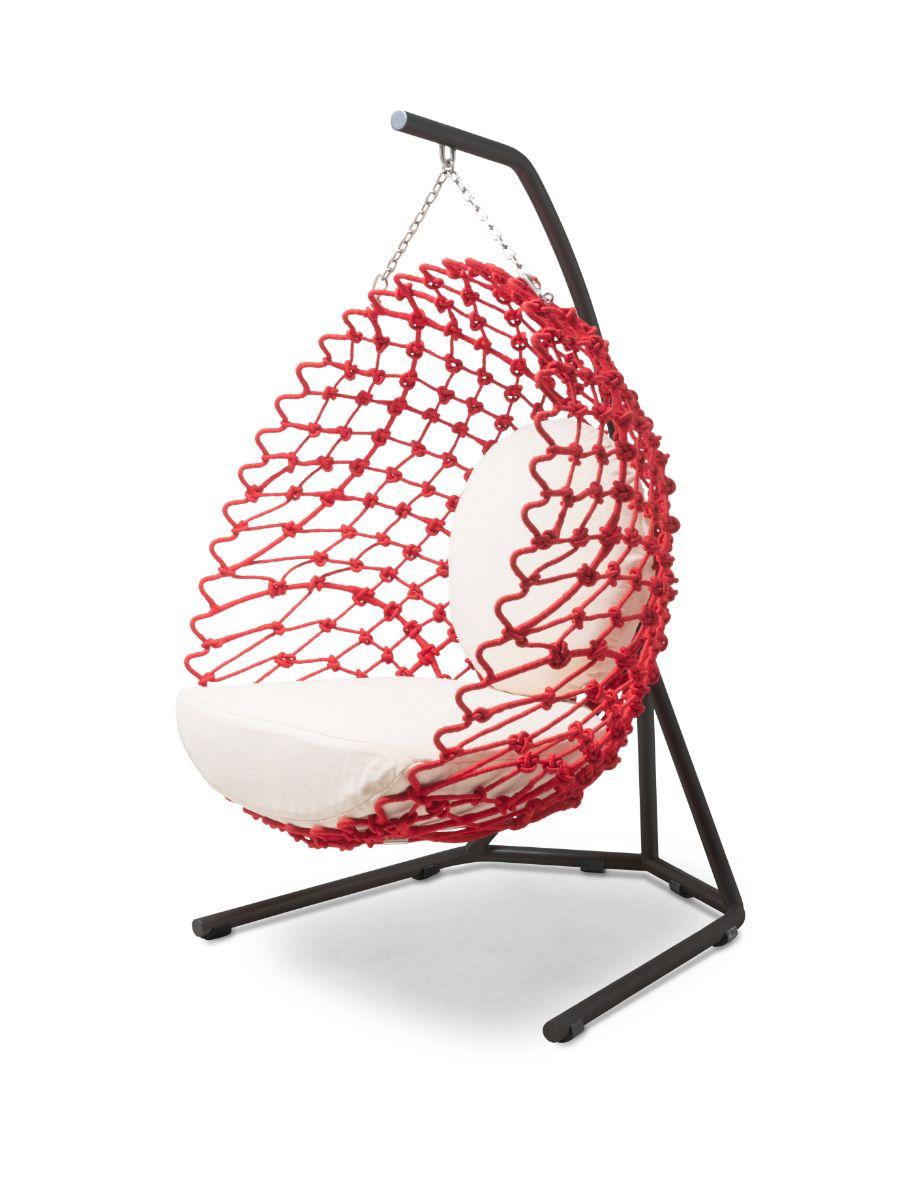 Red netted hanging chair with white cushion on a black stand against a white background