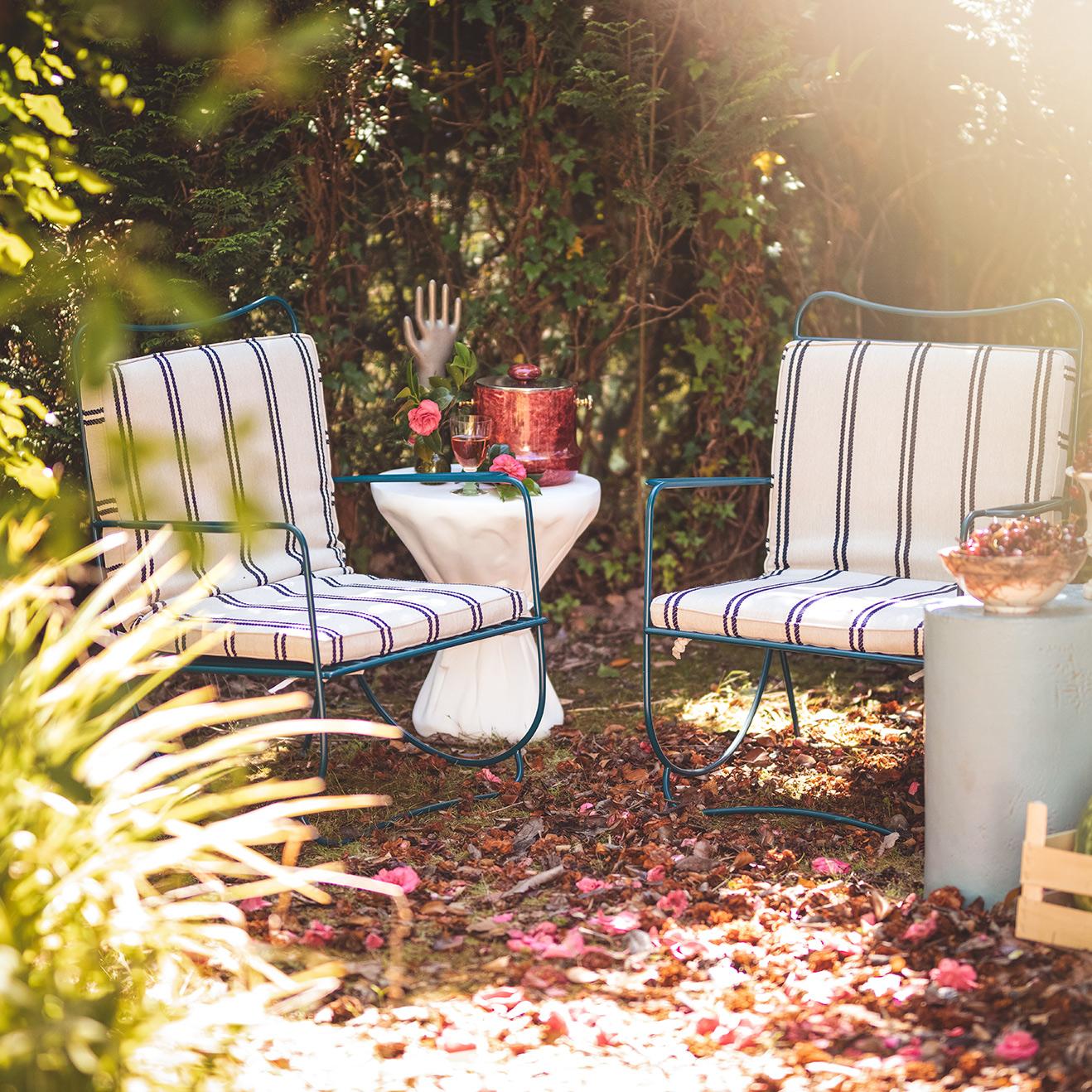 Two striped chairs with cushions in a garden setting with a small table and decorative items.
