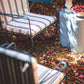 Two striped patio chairs with a small table holding decorative items on a leaf-covered ground.