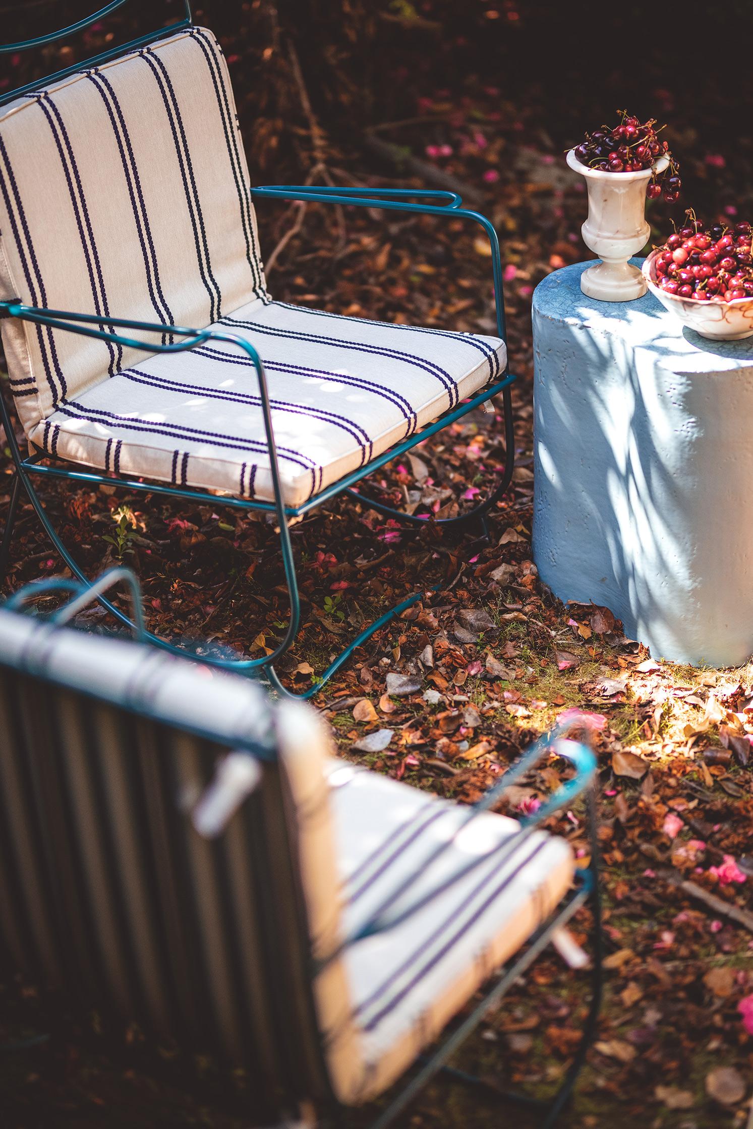 Two striped patio chairs with a small table holding decorative items on a leaf-covered ground.