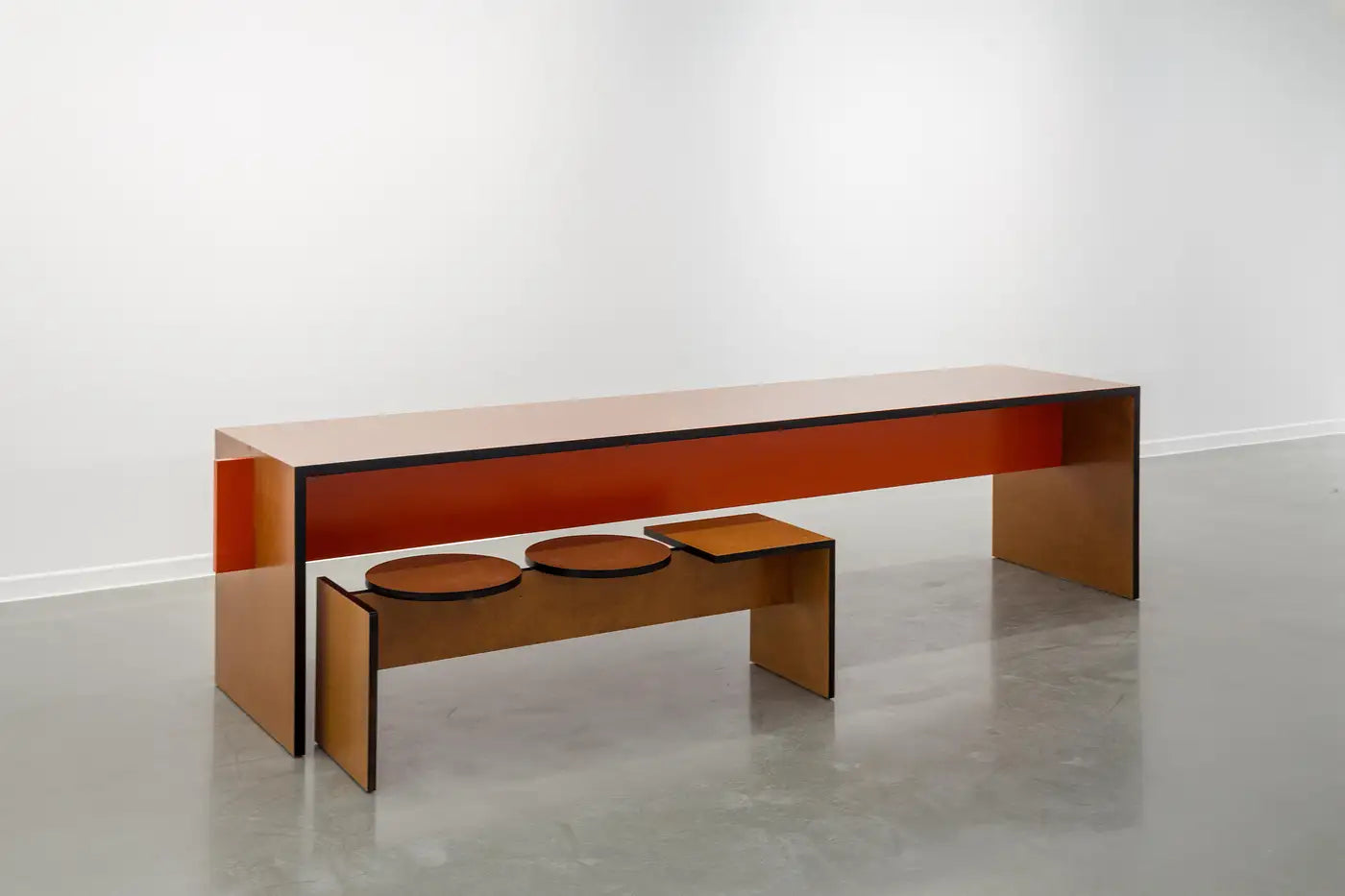 Modern wooden bench with three circular seats on a white floor and wall.