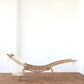 Wooden chaise lounge with white cushions against a white wall on a wooden floor