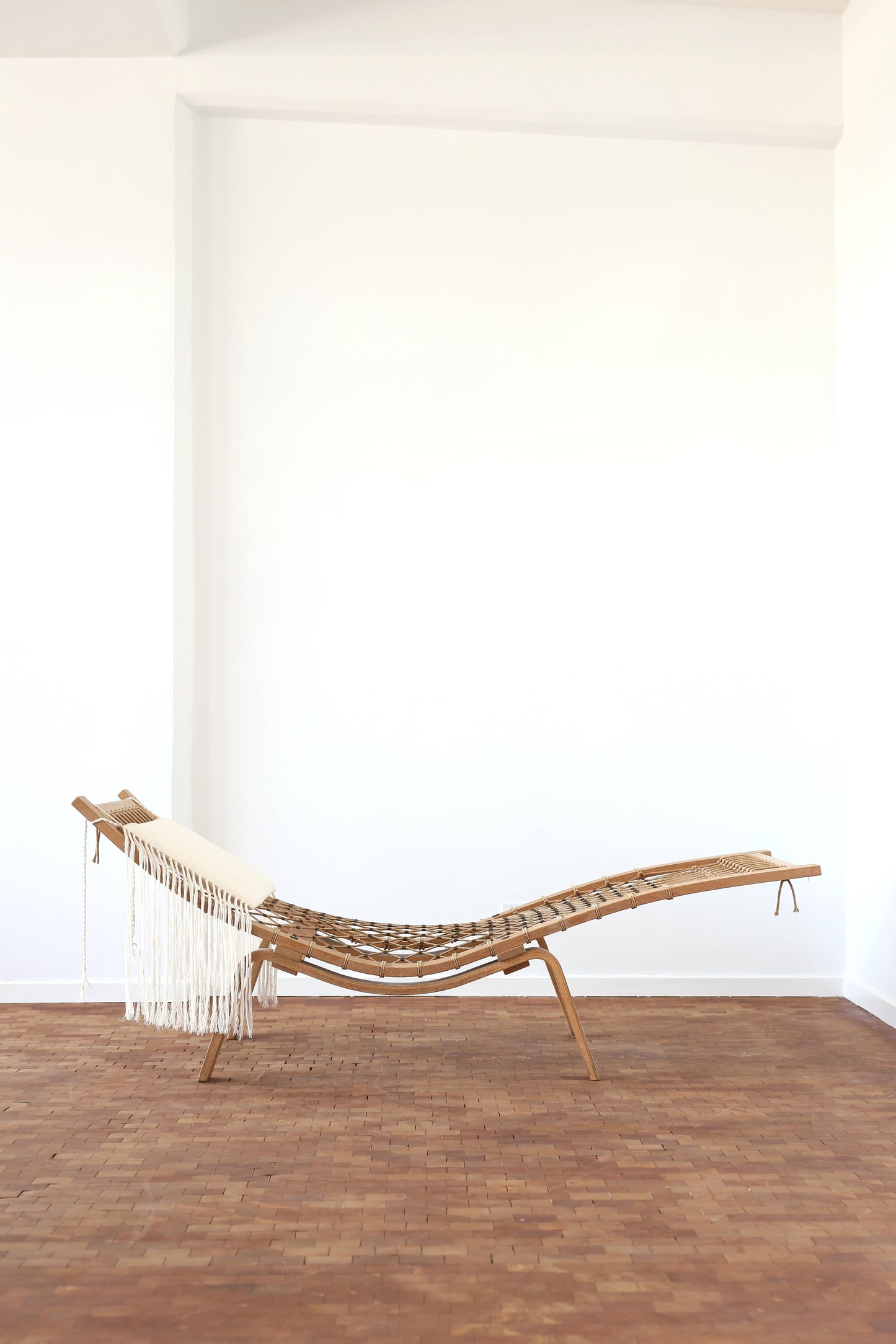 Wooden chaise lounge with white cushions against a white wall on a wooden floor