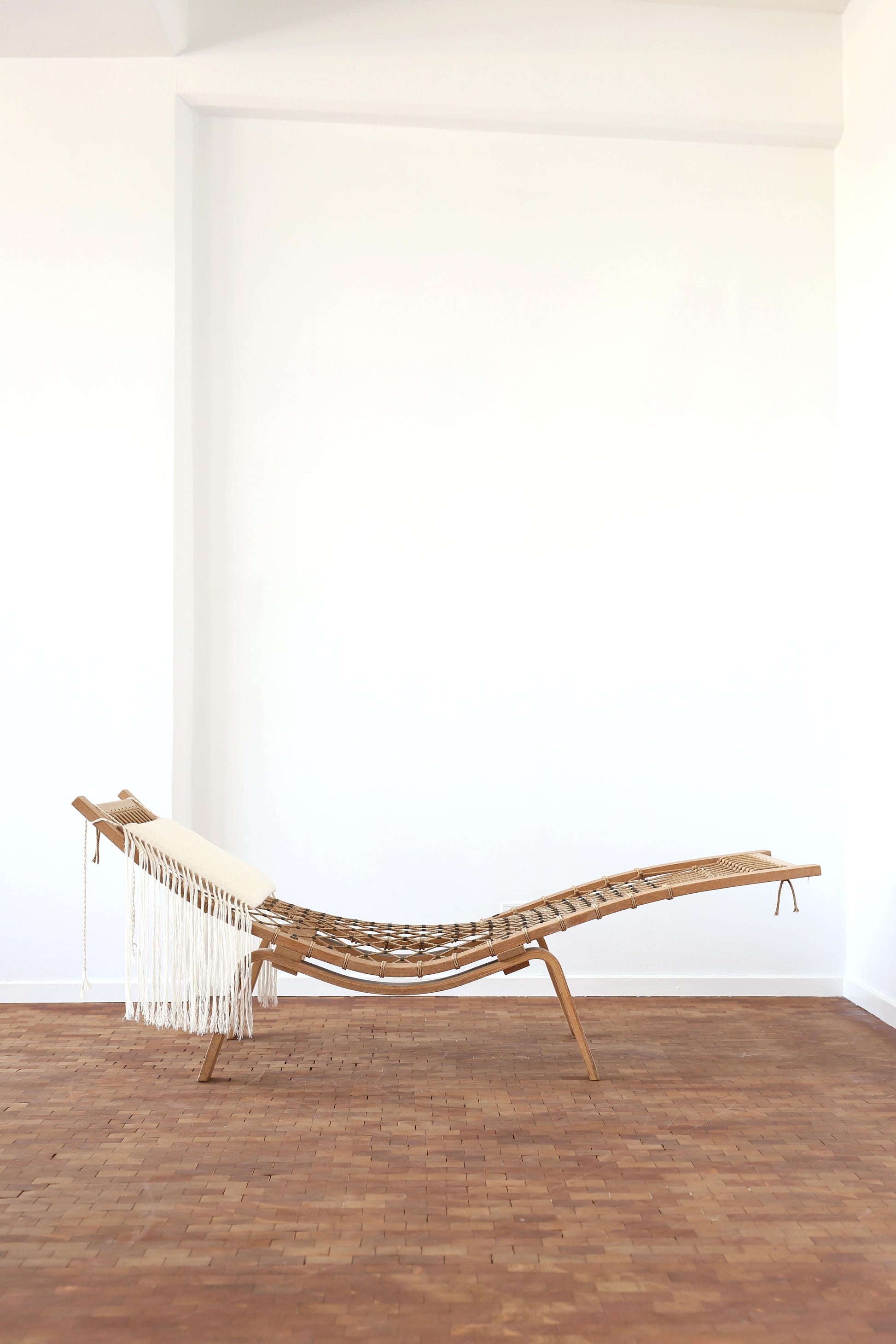 Wooden chaise lounge with white cushions against a white wall on a wooden floor