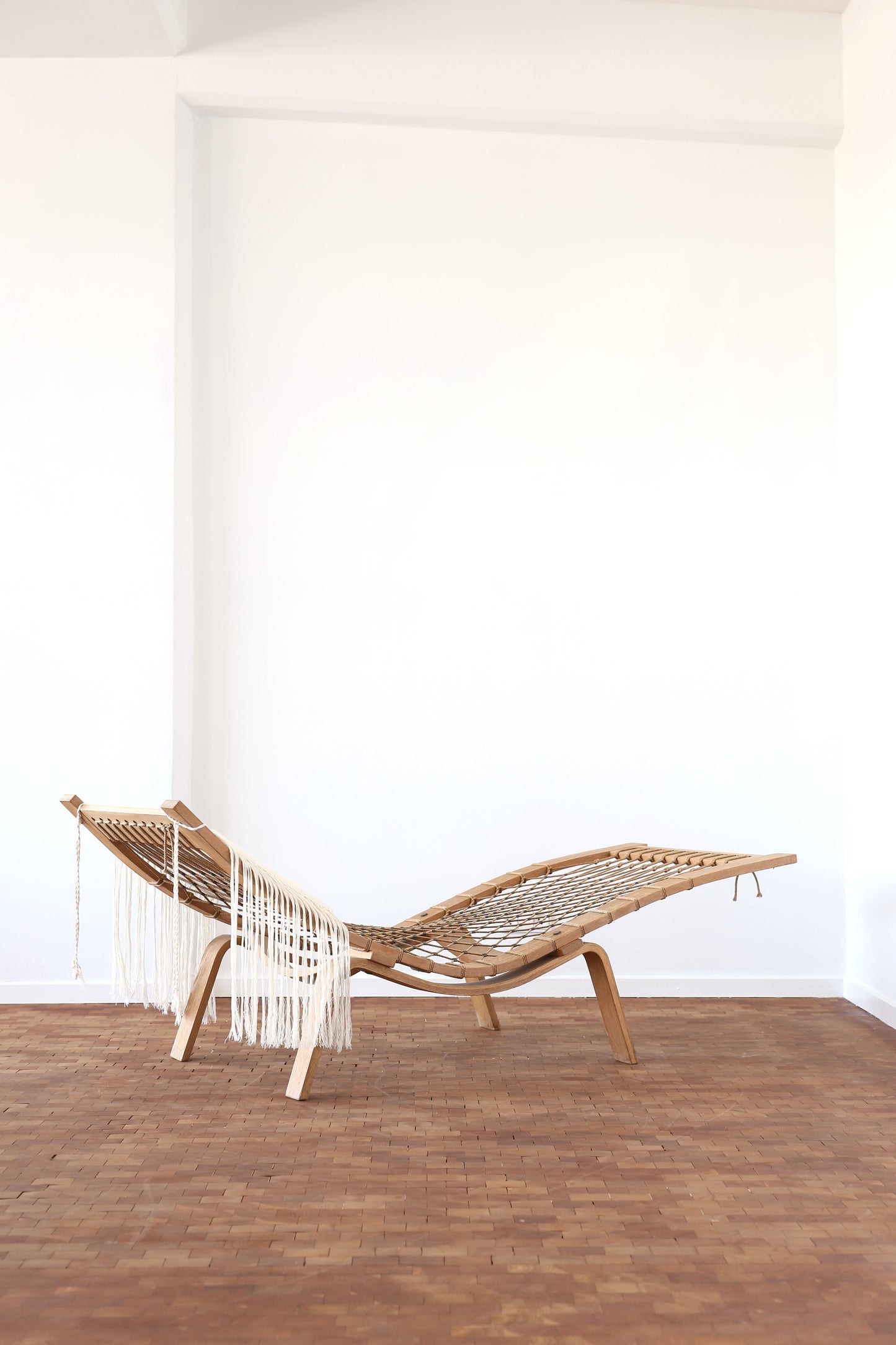 Woven chair with fringe on a wooden floor against a white wall