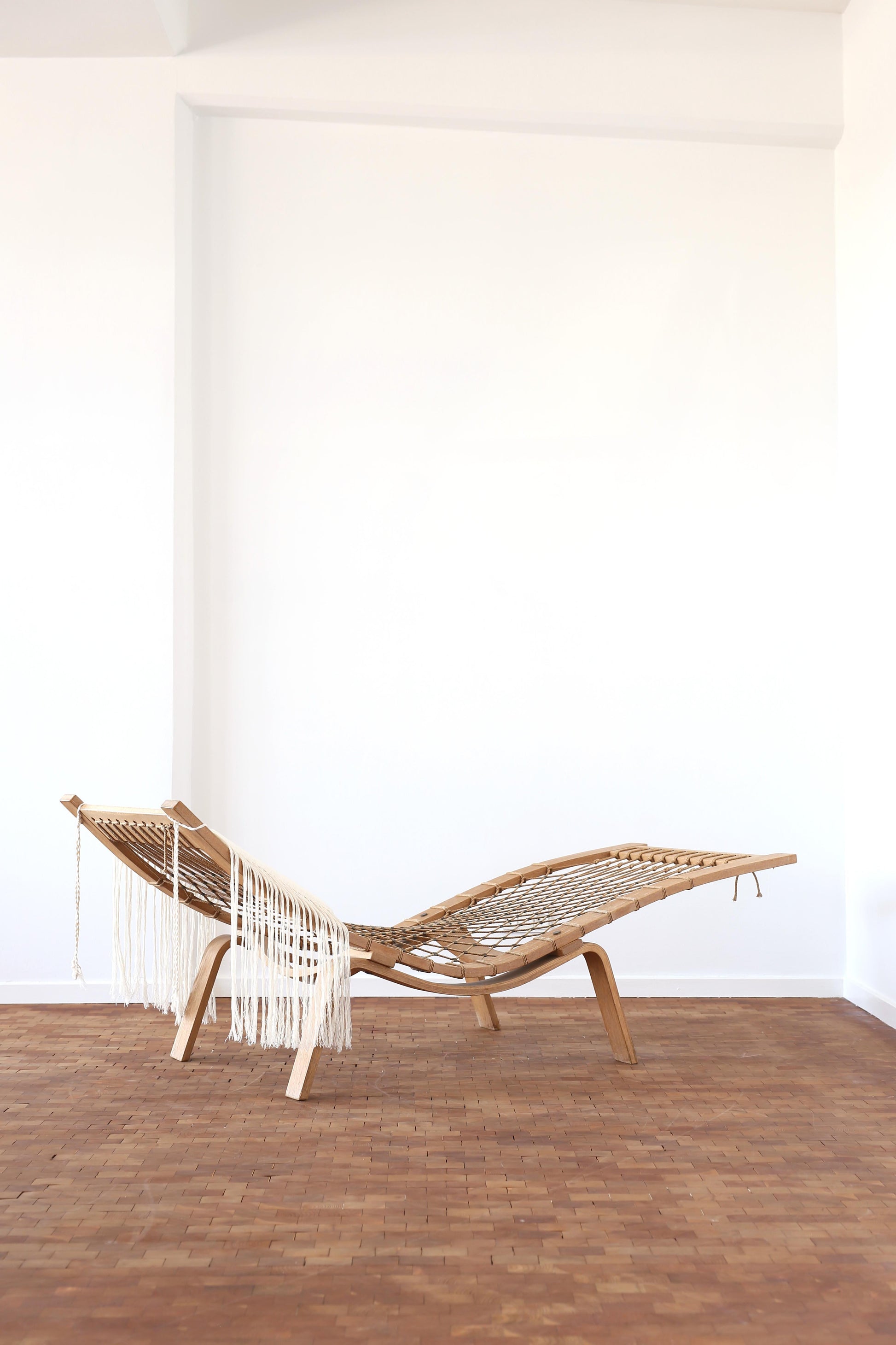 Woven chair with fringe on a wooden floor against a white wall