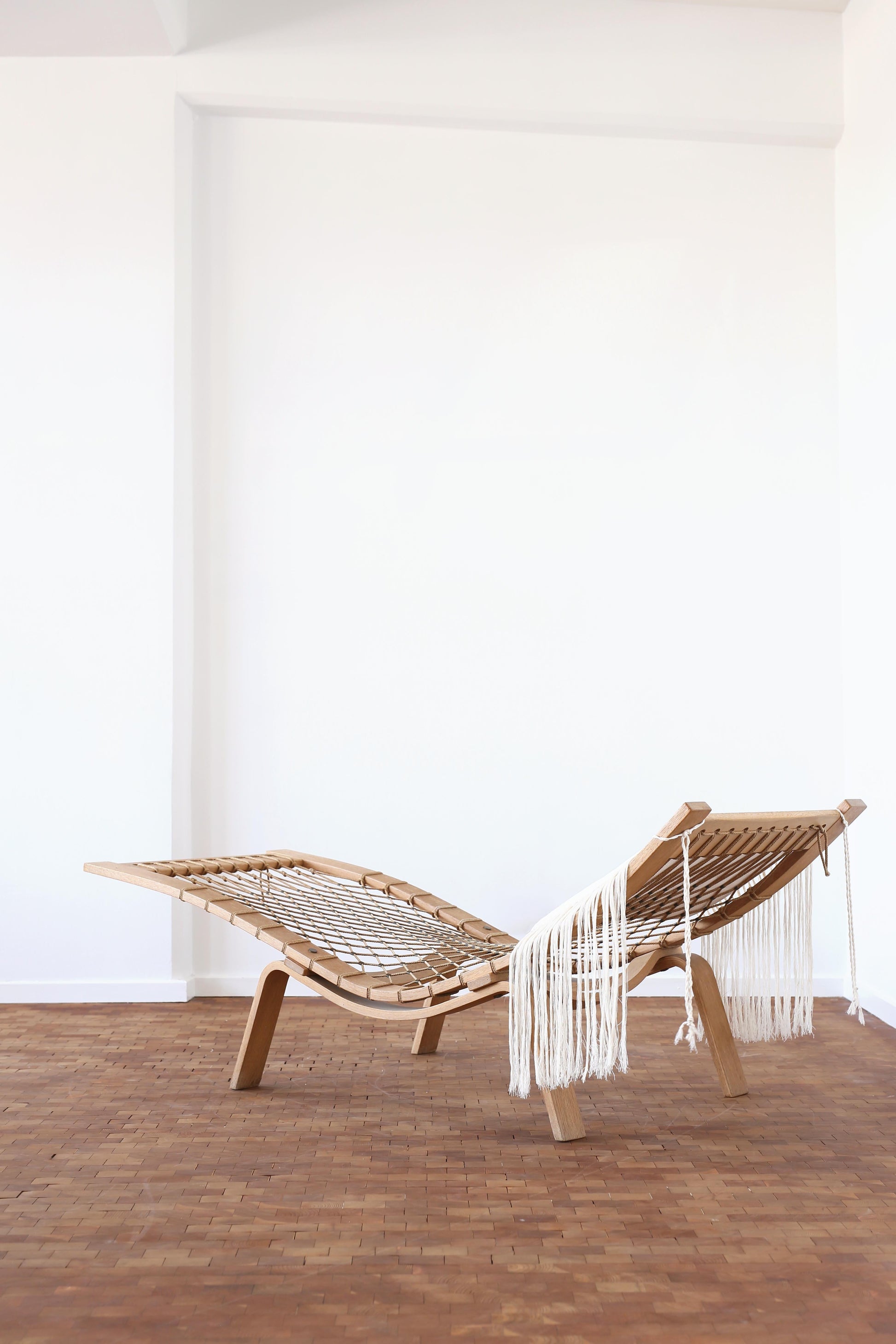 Wooden lounge chair with a white woven backrest in a minimalistic room.