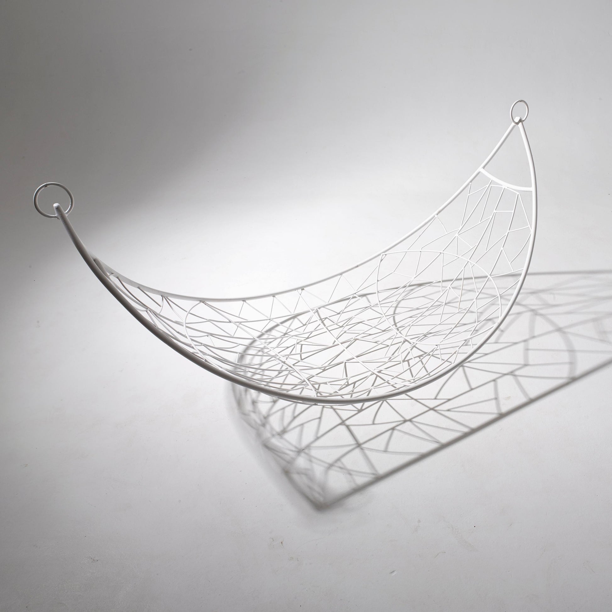 Wire hammock sculpture on a plain background