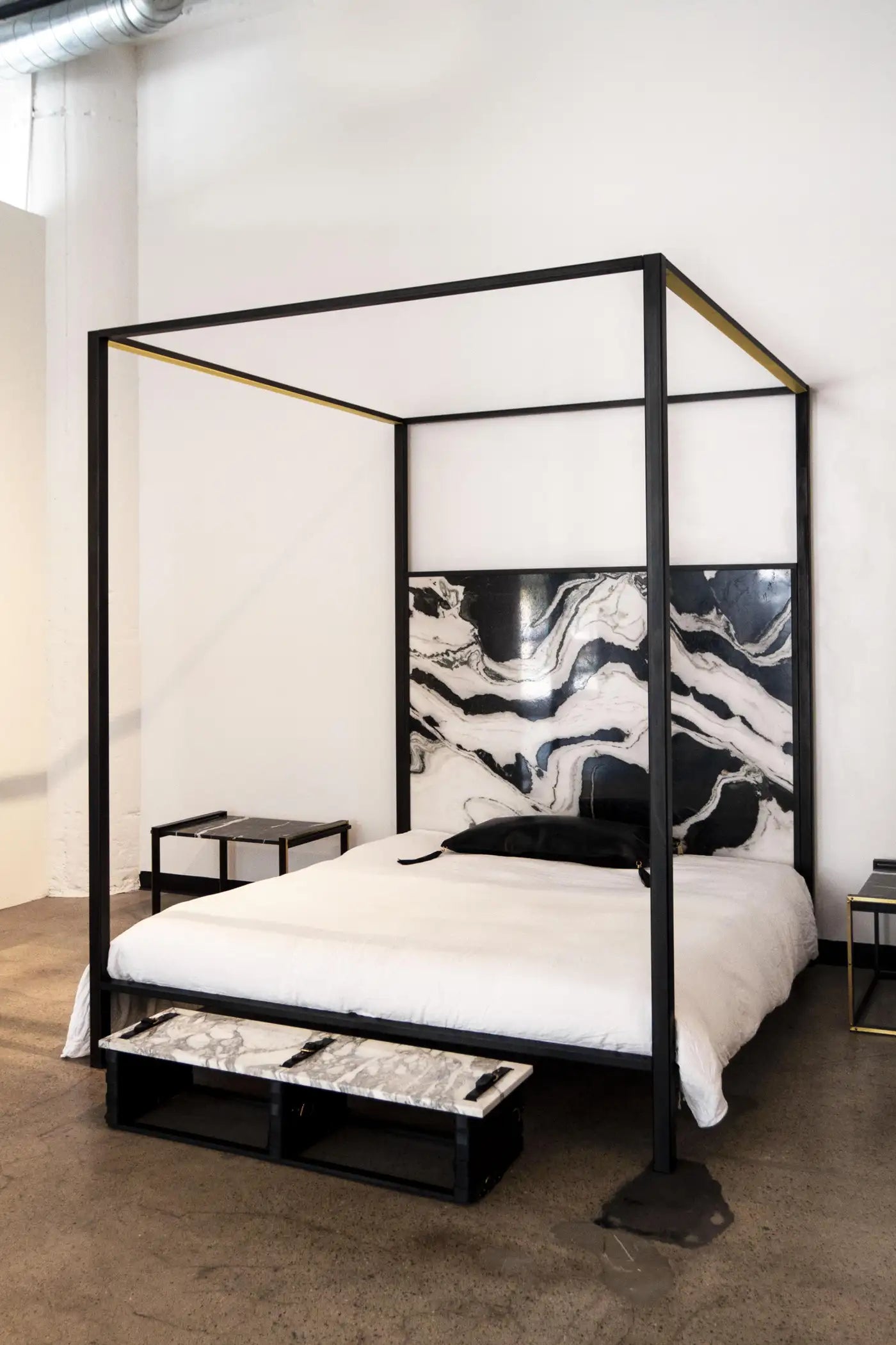 Modern bedroom with a black metal canopy bed and marble headboard.