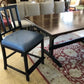 Dining table with chairs, including a blue cushioned chair, on a patterned rug.