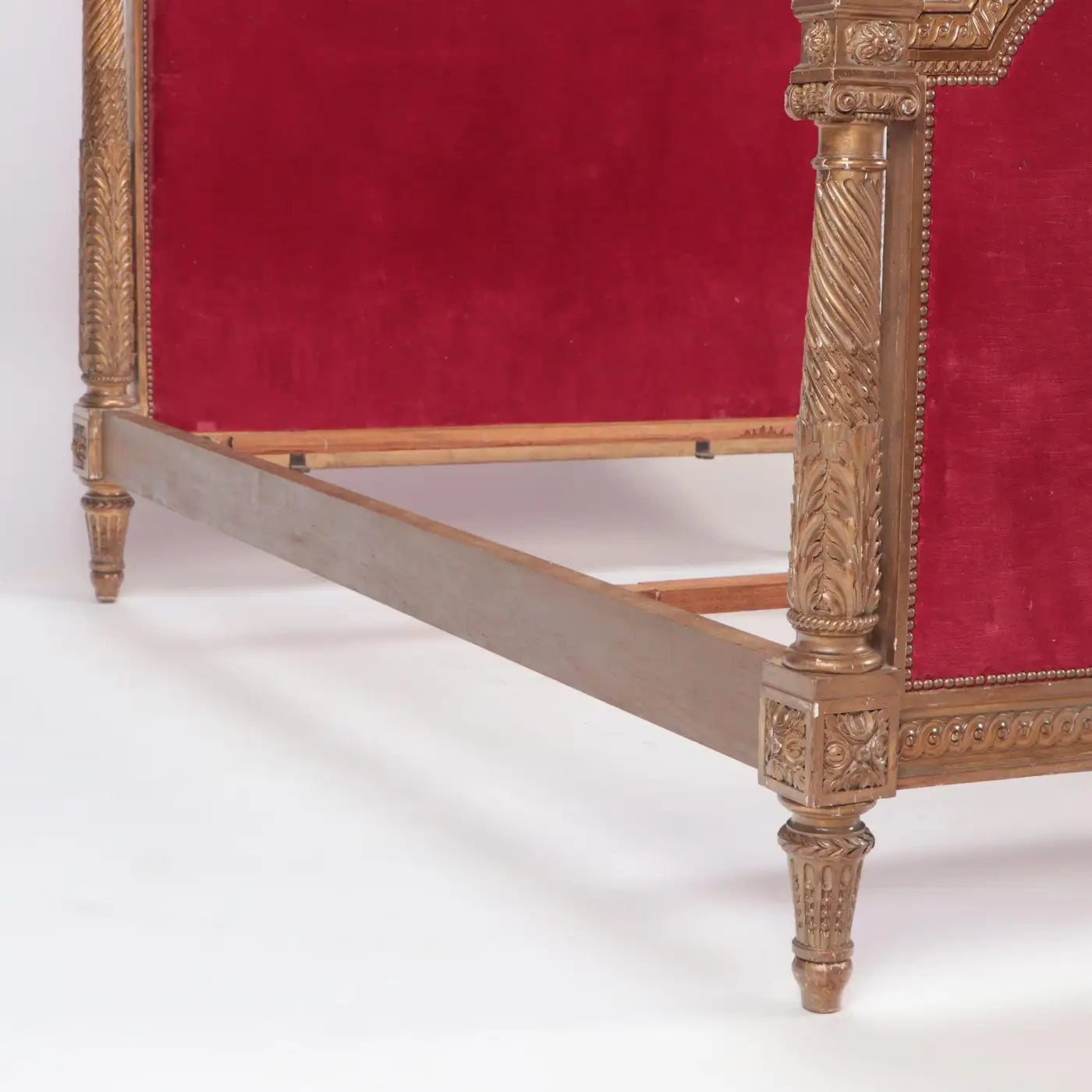 Decorative bed with gold frame and red velvet backrest on a white background