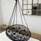 Black woven hanging chair in a room with a window and wooden floor.