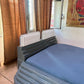 Bed with blue mattress in a room with brown curtains and a painting on the wall.