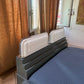 Bed with a white headboard in a room with brown curtains and a door.