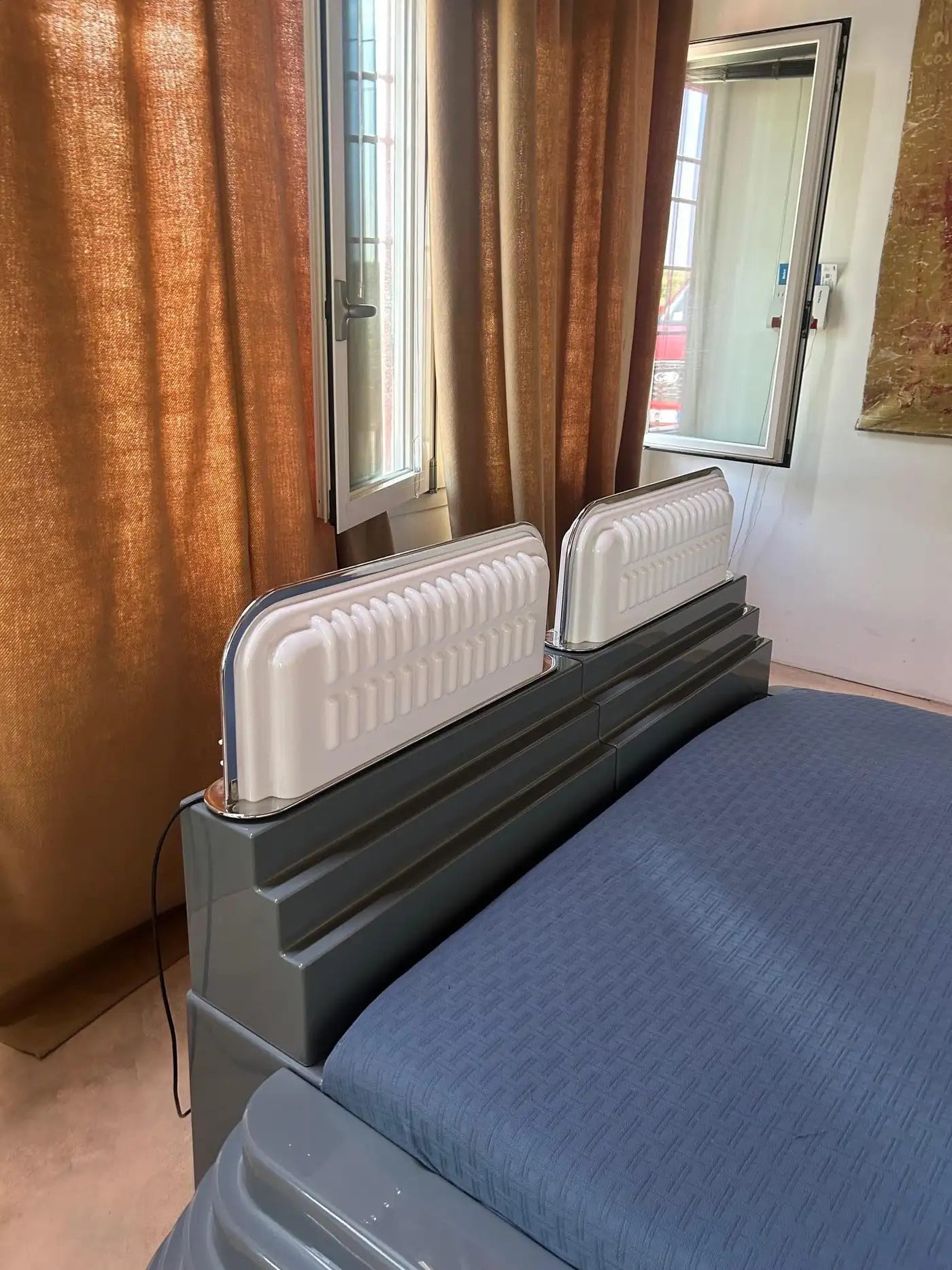 Bed with a white headboard in a room with brown curtains and a door.