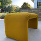 Yellow outdoor bench on a patio with trees and building in the background