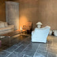 Living room with a beige sofa, white armchair, and wooden coffee table on a stone floor.