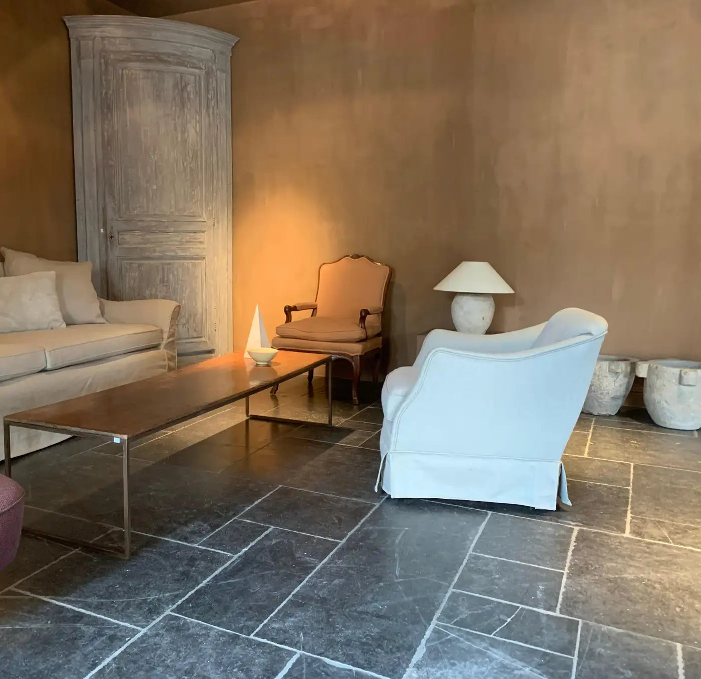Living room with a beige sofa, white armchair, and wooden coffee table on a stone floor.