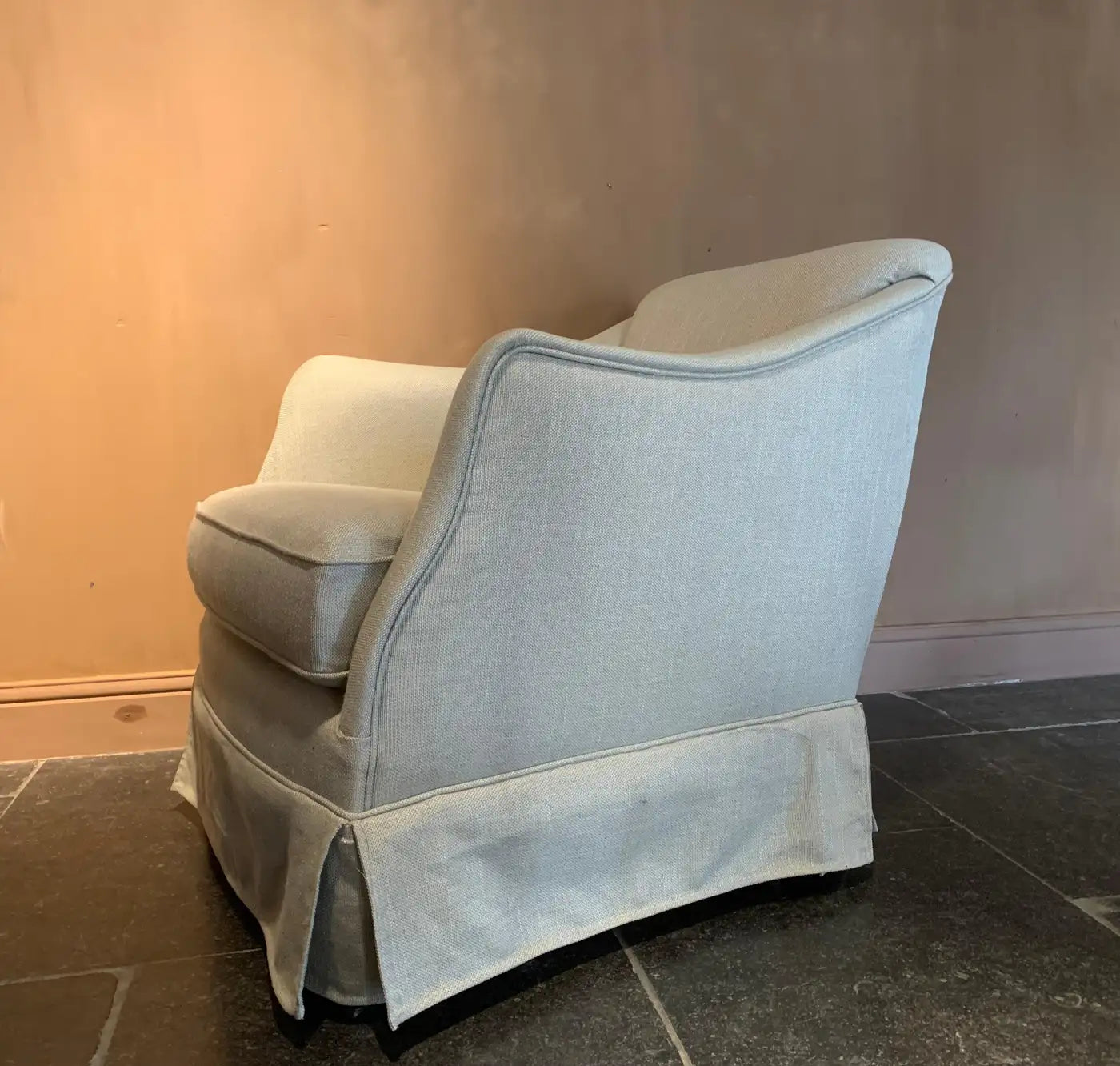 Light gray armchair against a plain wall with a tiled floor.