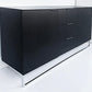 Black sideboard with drawers on a white floor and wall