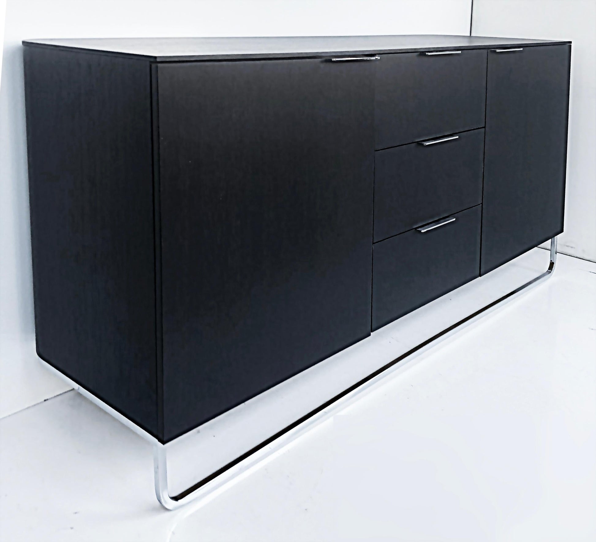 Black sideboard with drawers on a white floor and wall