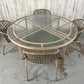 Round glass table with metal frame and four matching chairs on a concrete floor.