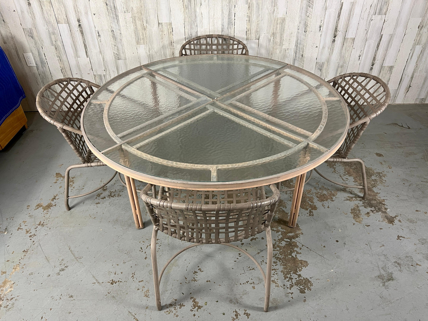 Round glass table with metal frame and four matching chairs on a concrete floor.