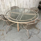 Round glass table with wicker chairs on a concrete floor against a wooden wall.