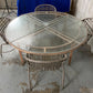 Round glass table with wicker chairs on a concrete floor.