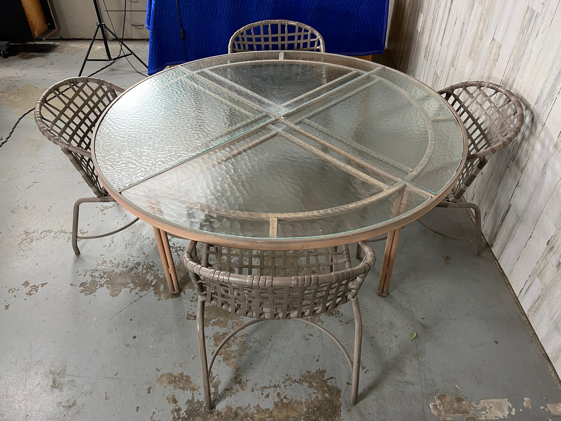 Round glass table with wicker chairs on a concrete floor.