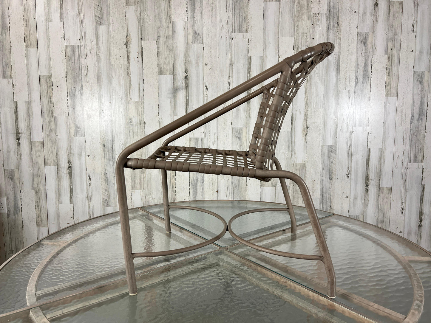 Wicker chair on a glass table against a wooden paneled wall