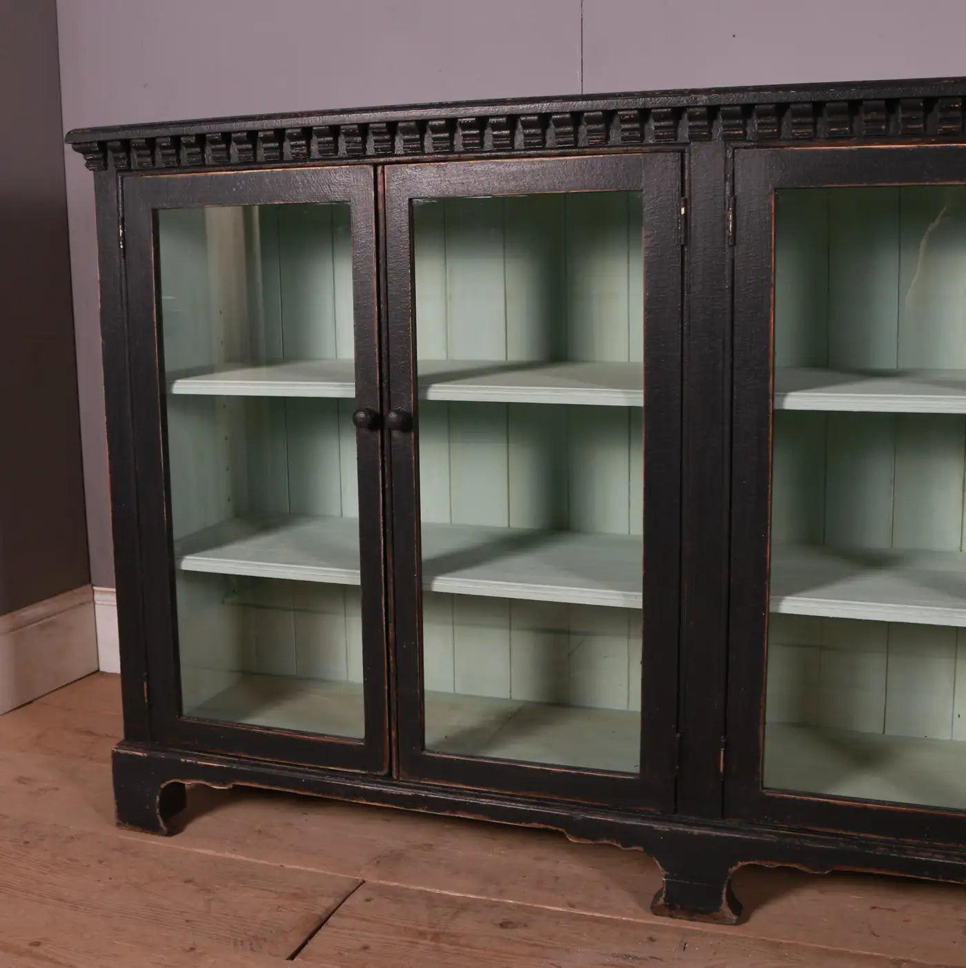 Vintage glass-fronted cabinet with dark wood frame on a wooden floor.