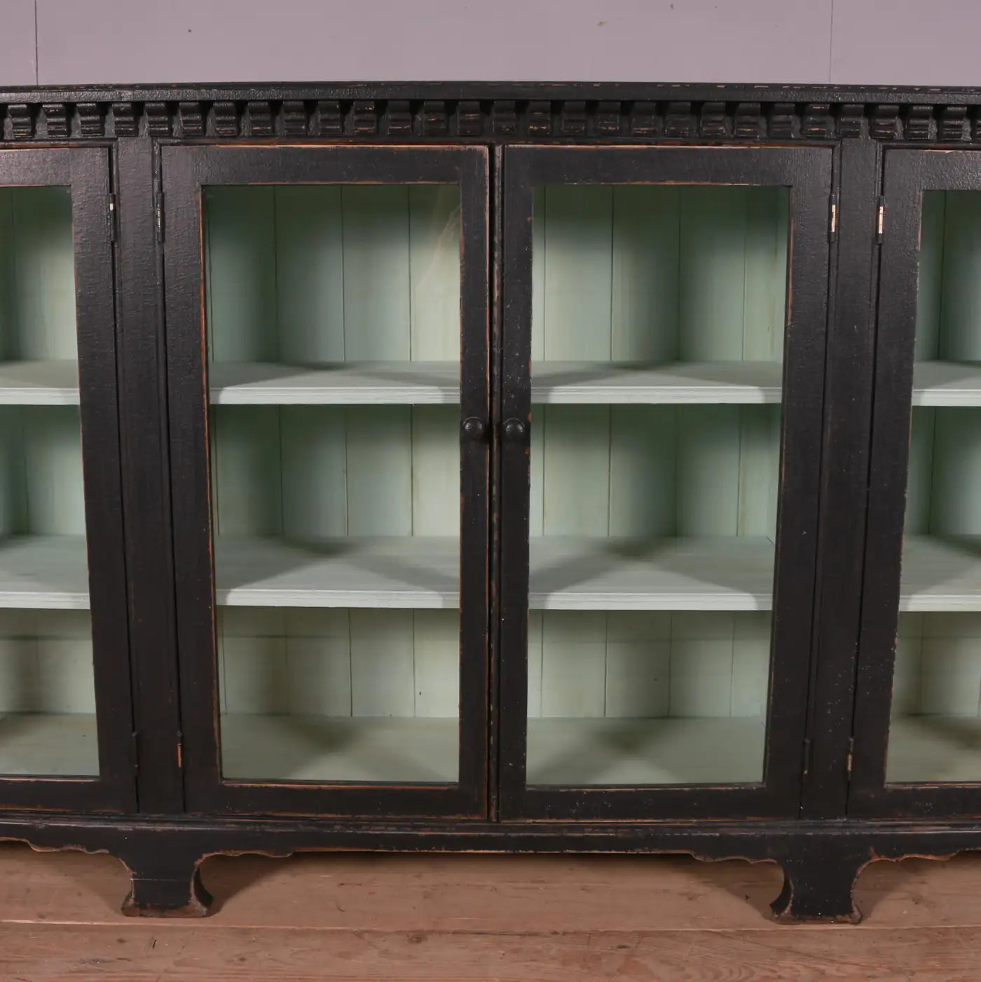 Vintage wooden cabinet with glass doors on a wooden floor.