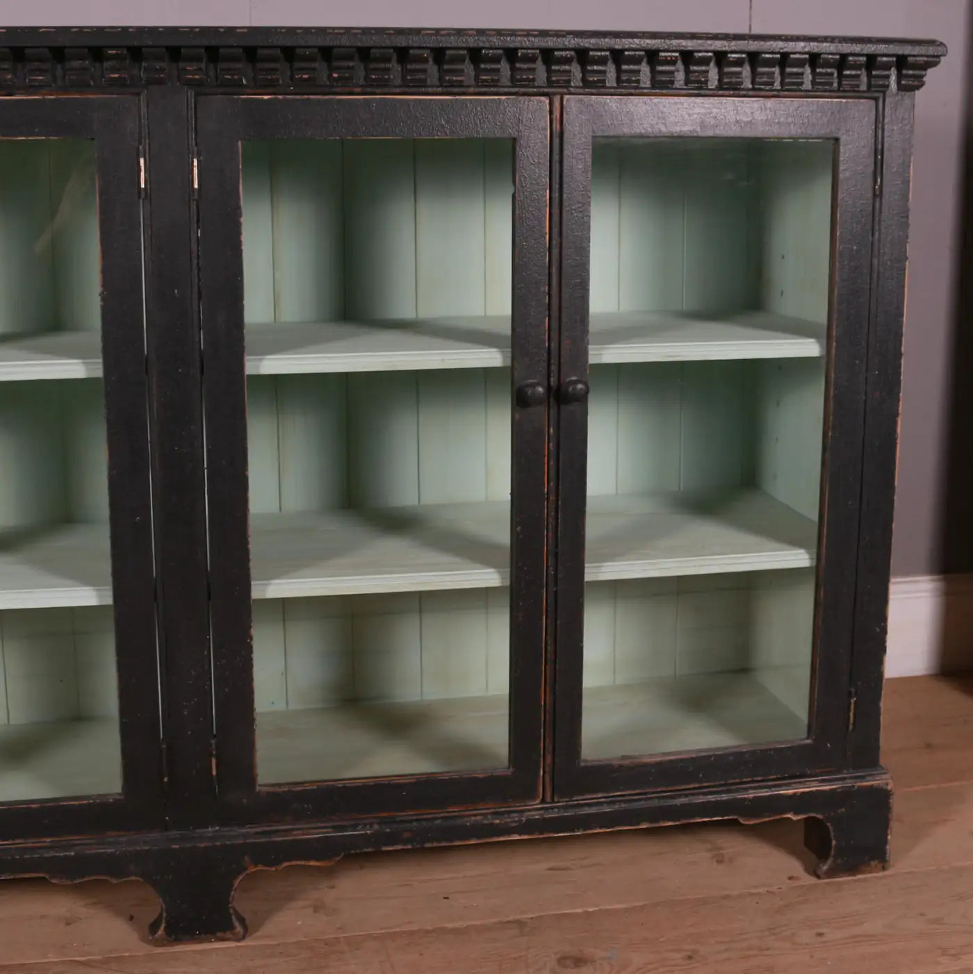 Vintage wooden cabinet with glass doors on a wooden floor.