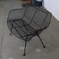 Black wire mesh chair on a concrete floor with a white wall in the background