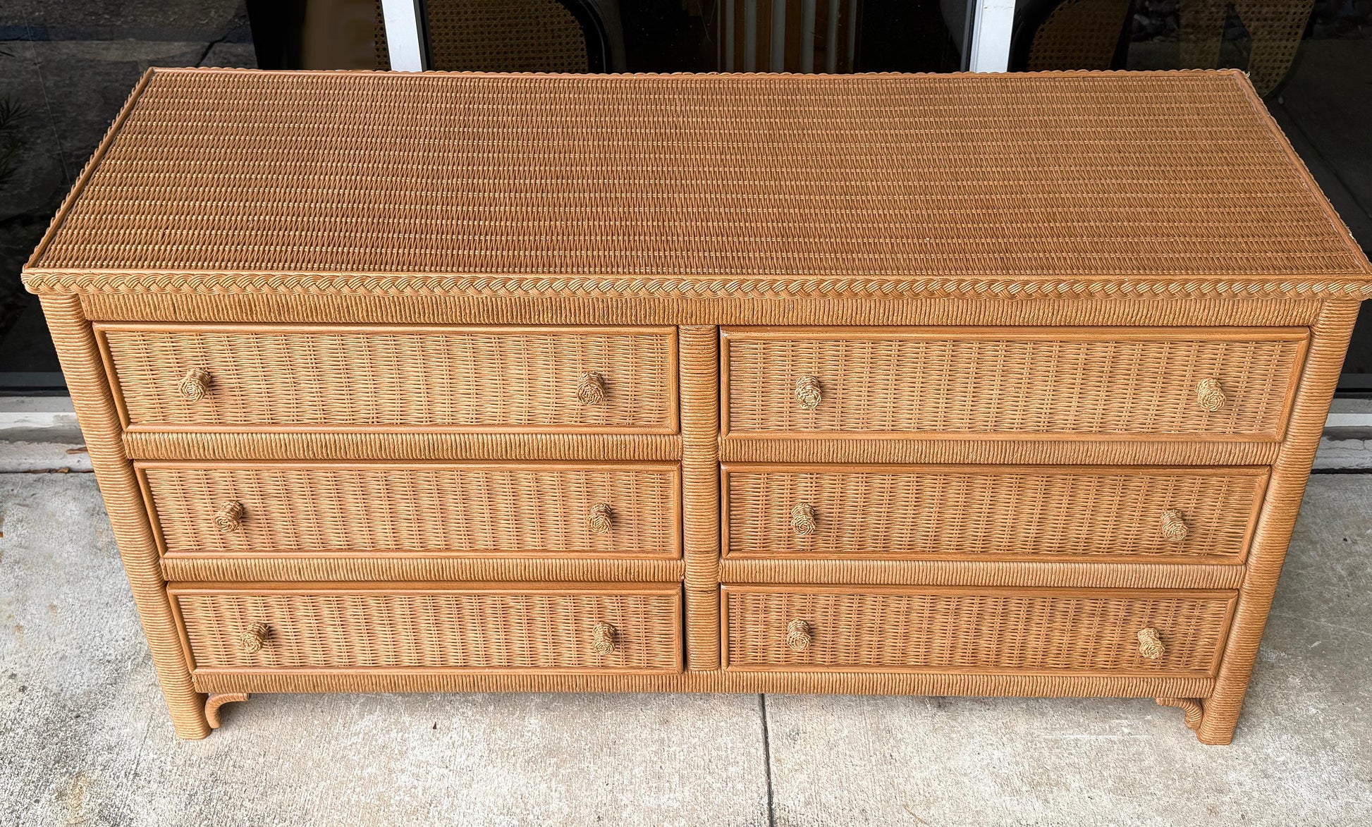Wicker dresser with multiple drawers on a concrete floor.