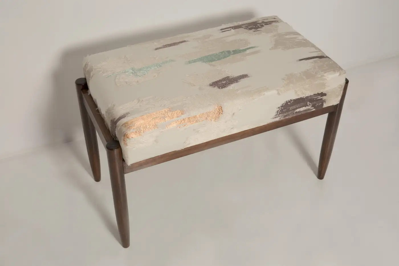 Small ottoman with patterned cushion on a plain background