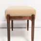Wooden stool with beige cushioned seat on a white background