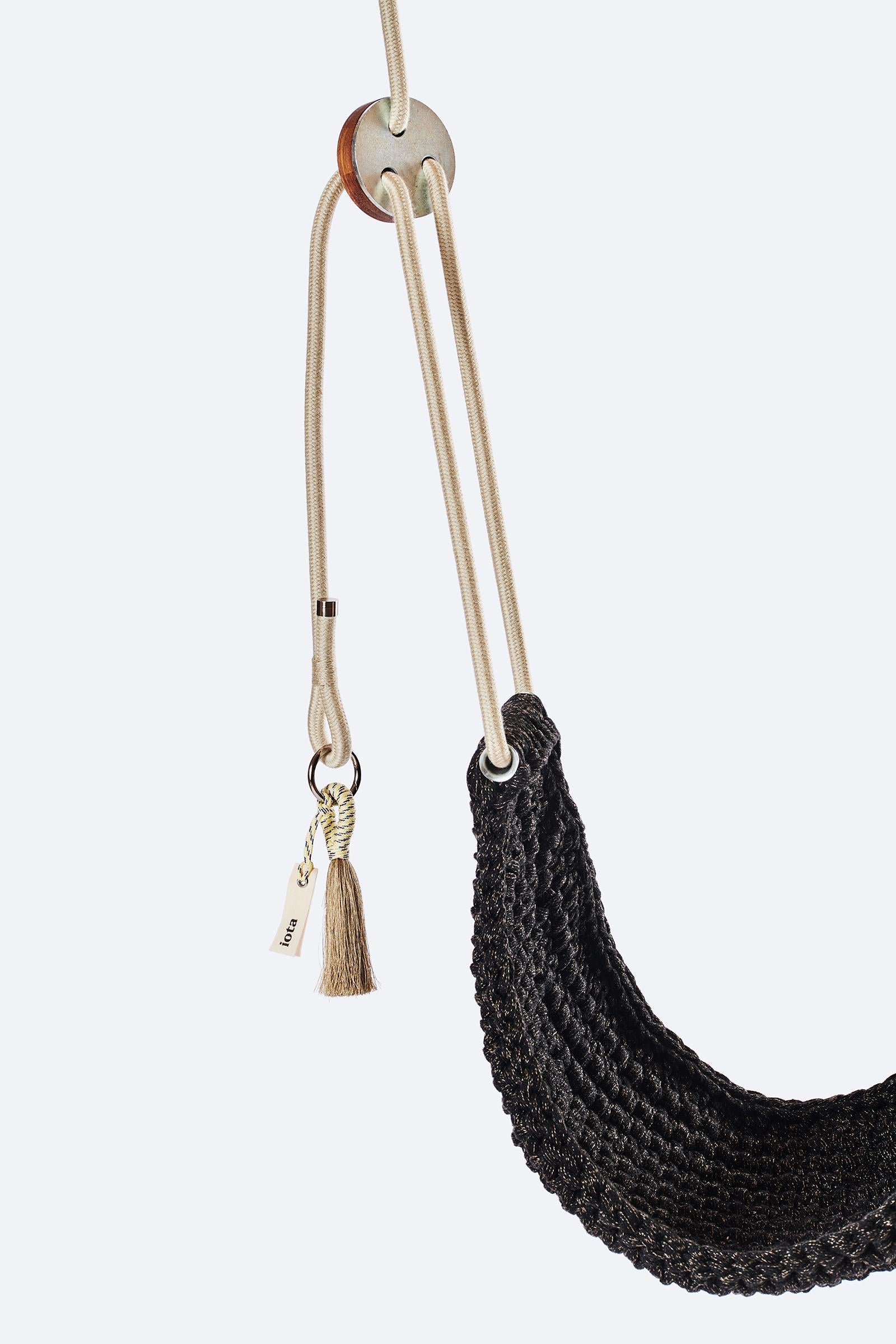 Black woven swing with beige ropes and tassels on a white background