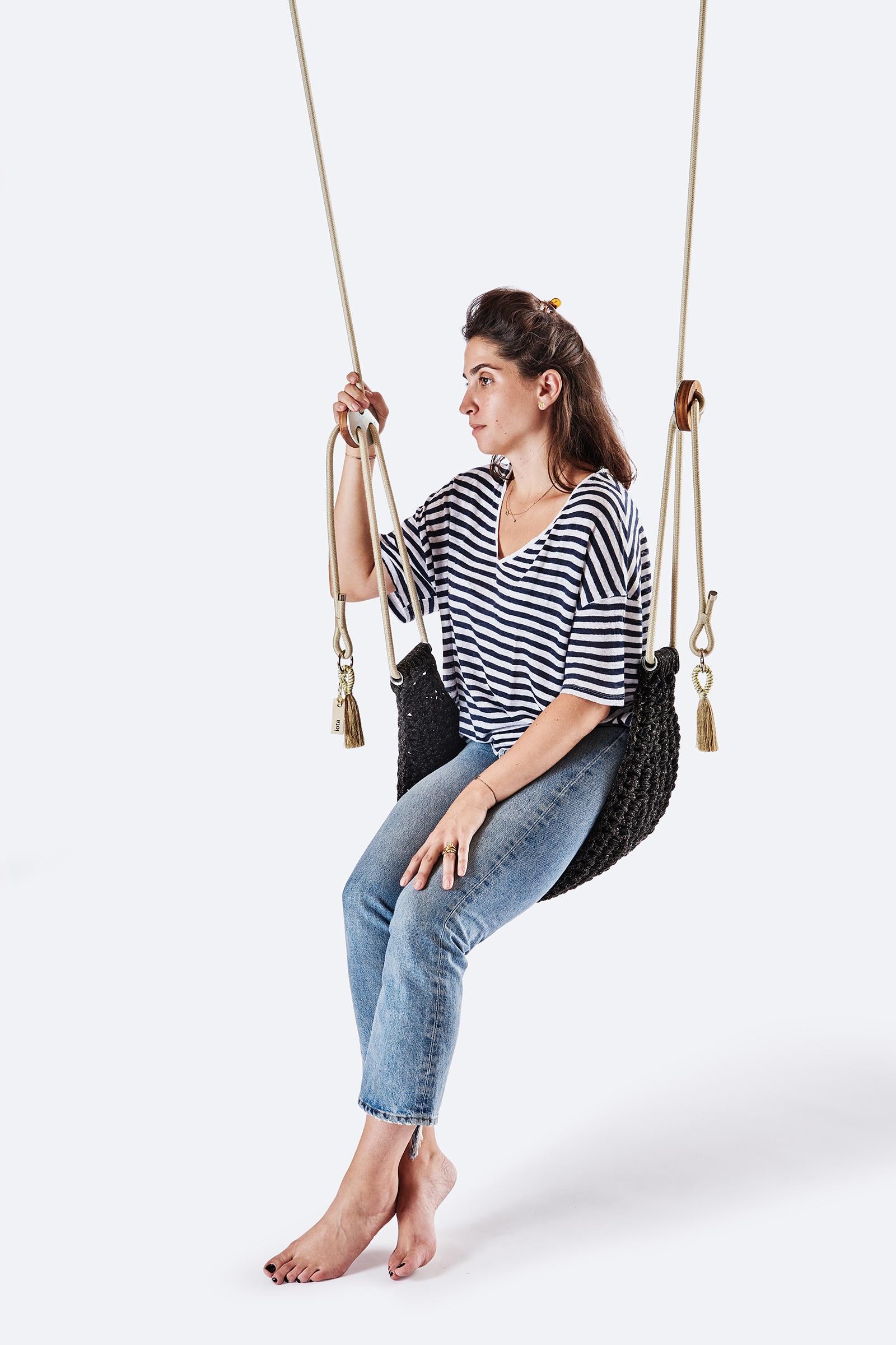 Woman sitting on a black woven swing against a white background