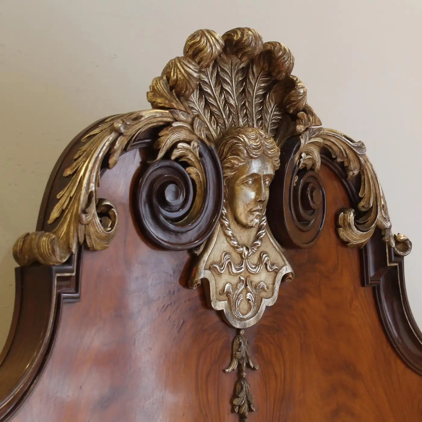 Decorative wooden headboard with gold leaf and face carvings on a beige wall.