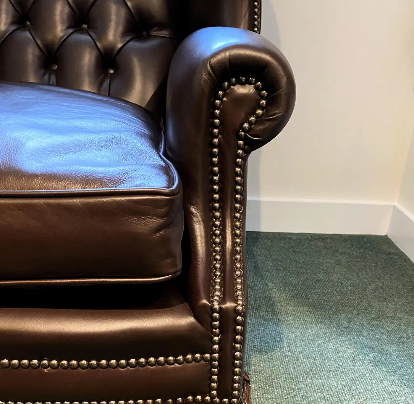 Brown leather armchair with tufted backrest and nailhead trim on a green carpet.