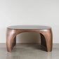Modern coffee table with wooden base and glass top on a concrete floor.