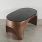 Modern wooden side table with a black top on a concrete floor.