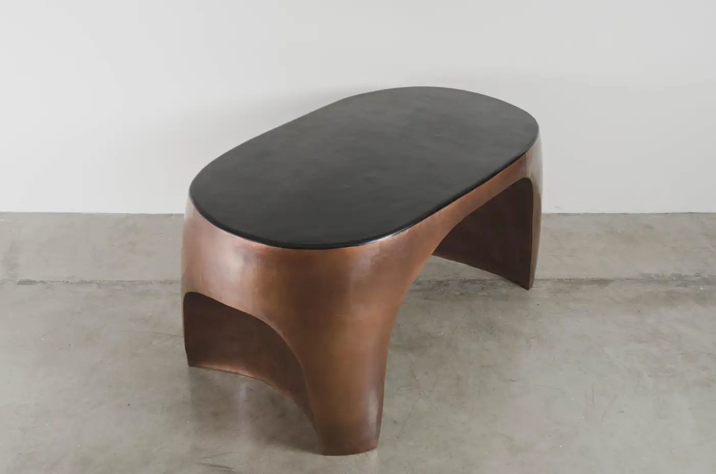 Modern wooden side table with a black top on a concrete floor.