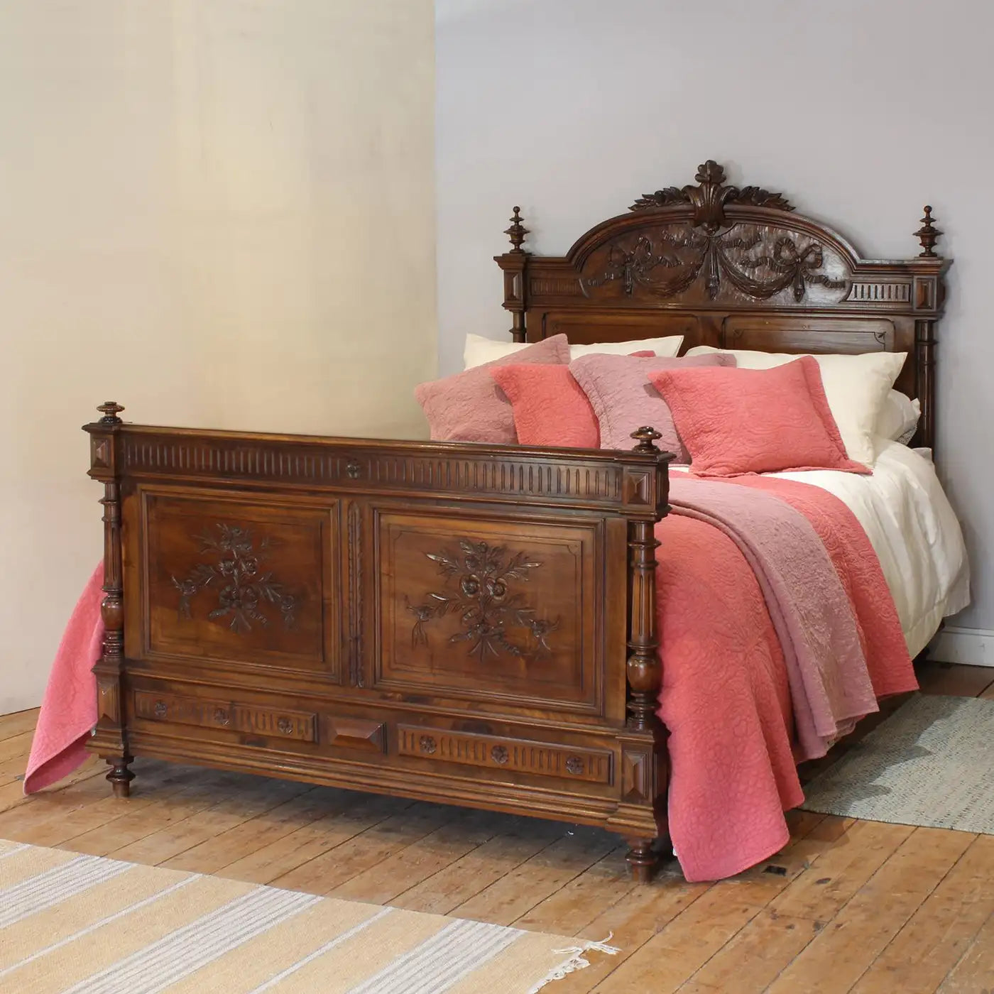 Wooden bed with pink bedding in a room with wooden flooring.