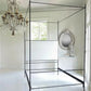 Black metal canopy bed in a bright bedroom with a chandelier and mirror.